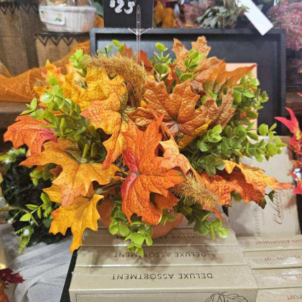 Autumn arrangement with orange maple leaves and green foliage in a container.