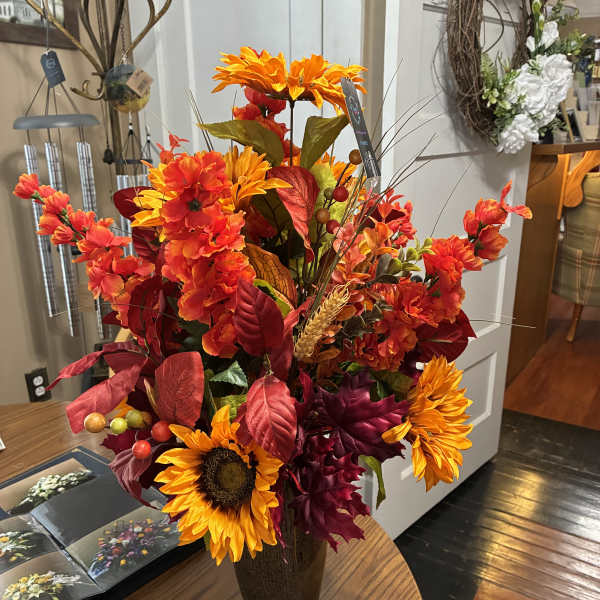 Tall autumn floral arrangement in a dark vase with orange and red blooms