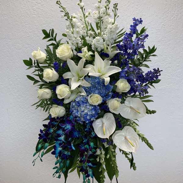 Standing floral spray with white lilies, roses, blue hydrangeas, and purple orchids