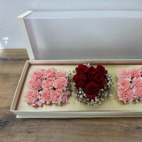 Open gift box with pink carnations and red roses arranged in three sections