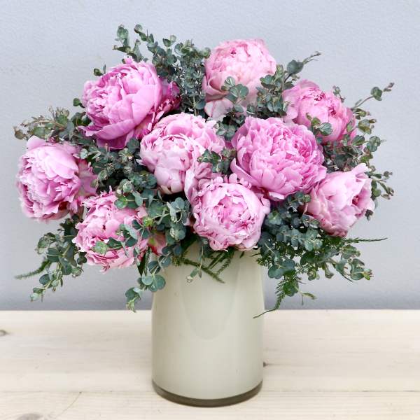 Arrangement of pink peonies with filler in a light cream cylinder vase