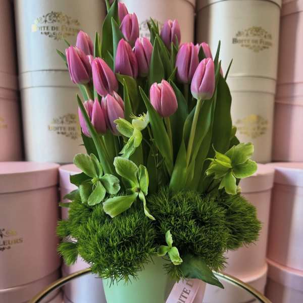 Pink tulips arranged in a pale green vase with green blooms