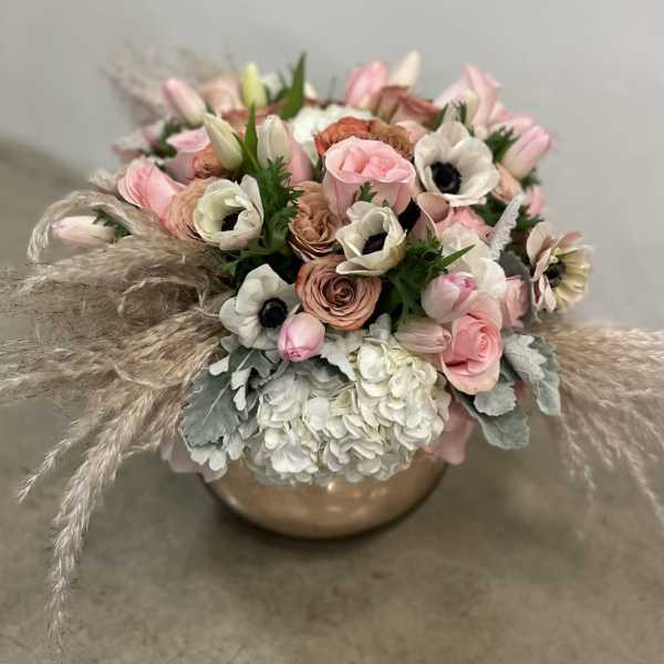 Low bowl arrangement of pink roses, white hydrangeas, anemones, tulips, and pampas plumes