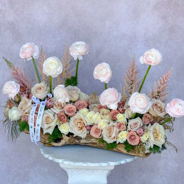 Long floral arrangement of pale roses and ranunculus in a wood container