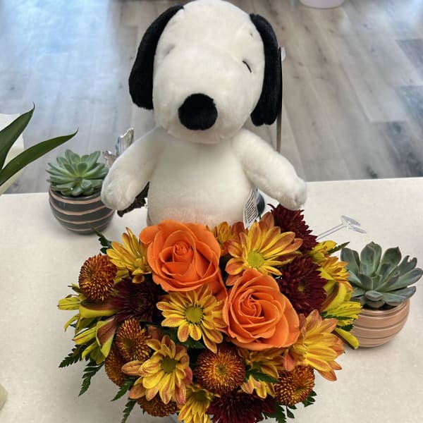 Orange roses and yellow chrysanthemums in a low arrangement with a plush Snoopy toy behind it