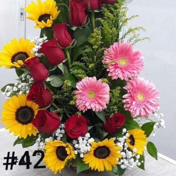 Tall floral arrangement with sunflowers, red roses, and pink gerbera daisies