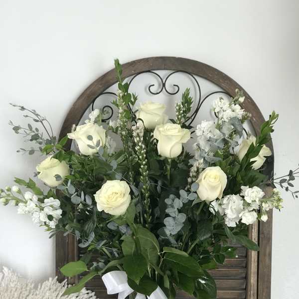 White roses and white filler flowers in a glass vase with greenery