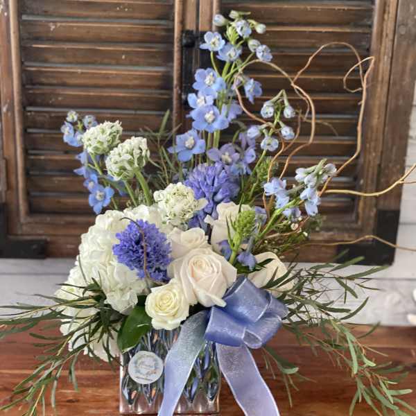 Blue and white floral arrangement in a glass vase with a ribbon