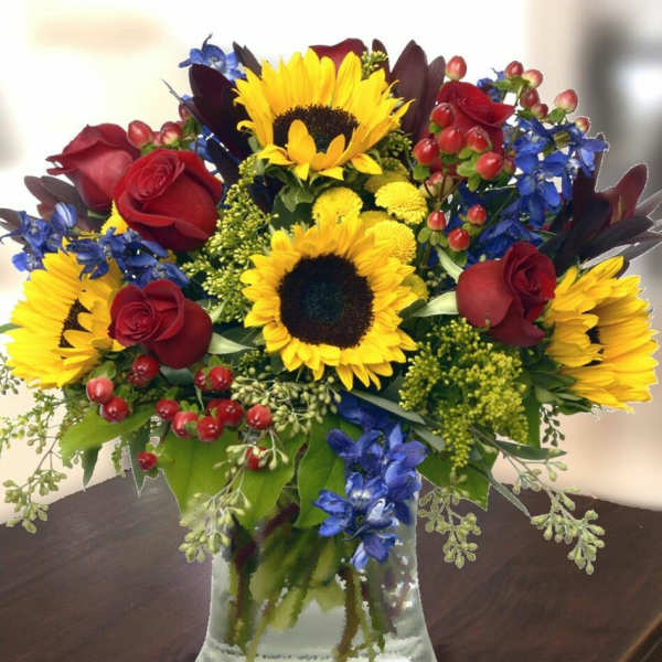 Bouquet of sunflowers, red roses, and blue flowers in a glass vase