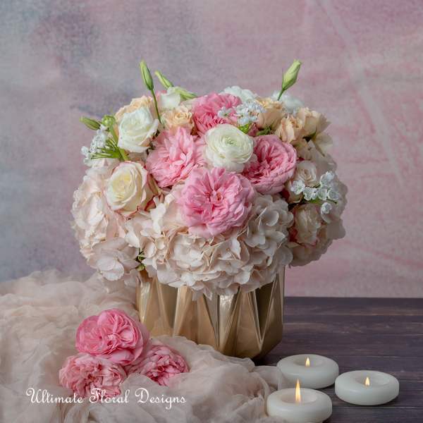 Pink and white floral arrangement in a gold vase with candles nearby