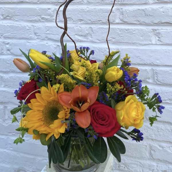 Colorful mixed flower arrangement in a glass vase with a bird ornament