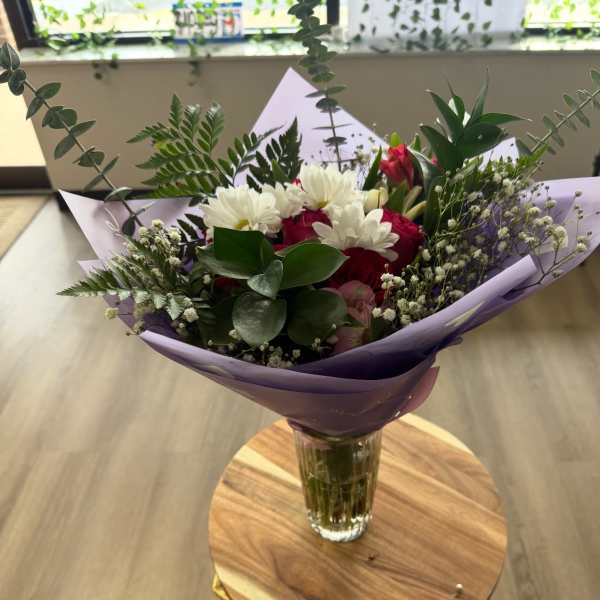 Bouquet of red and white flowers in purple wrap with a glass vase