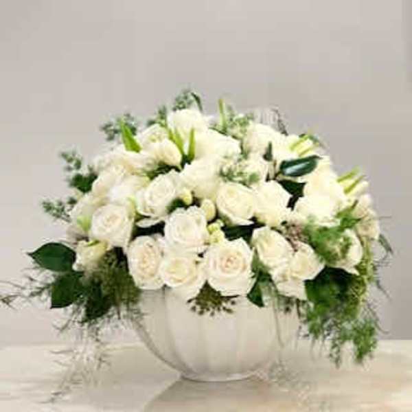 White rose arrangement in a white vase with trailing greenery