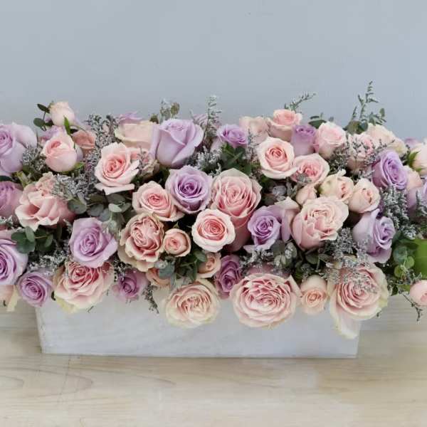 Pink and lavender roses arranged in a white rectangular container
