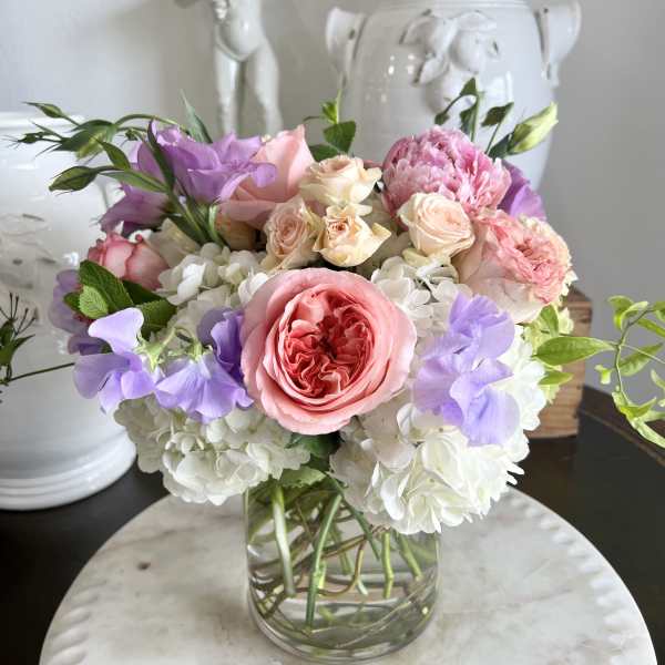 Pastel bouquet of roses, hydrangeas, and purple blooms in a glass vase