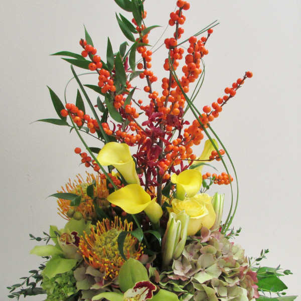 Tall floral arrangement with yellow calla lilies, orange berries, and hydrangeas in a white container