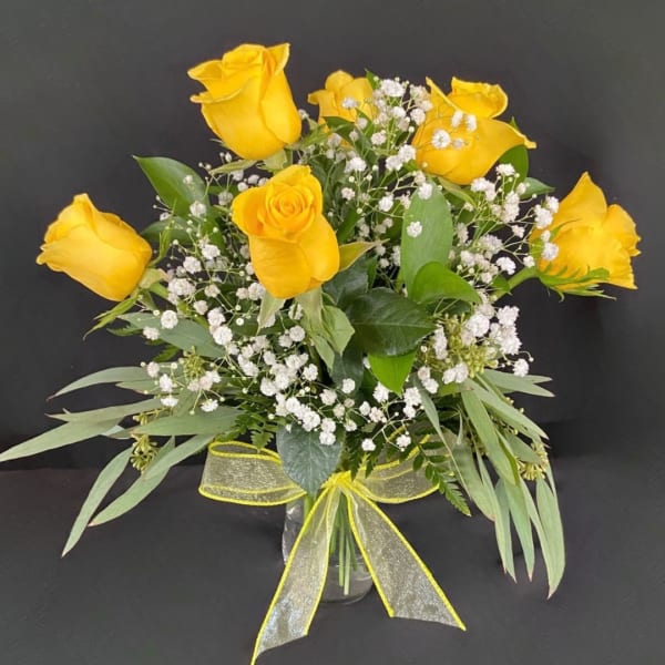 Yellow roses arranged in a clear vase with baby's breath and a yellow ribbon.