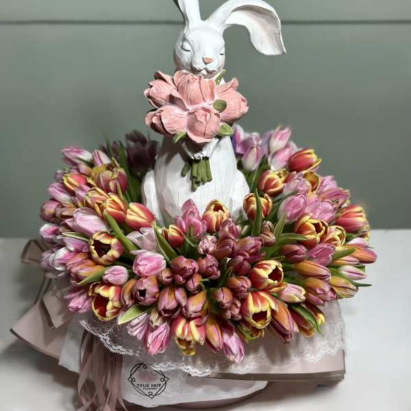 White rabbit figurine holding pink flowers, surrounded by a ring of pink and yellow tulips