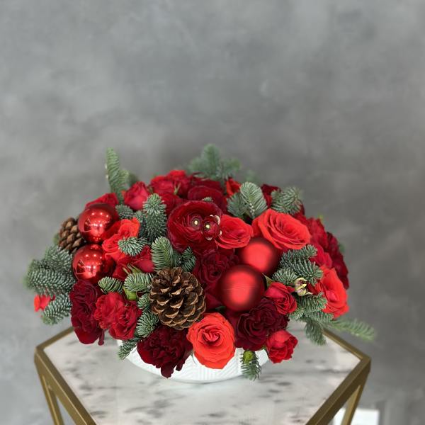 Red rose arrangement with pinecones and red ornaments in a white bowl