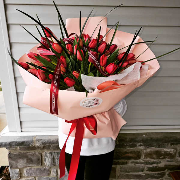 Large bouquet of red tulips wrapped in pale pink paper with a red ribbon
