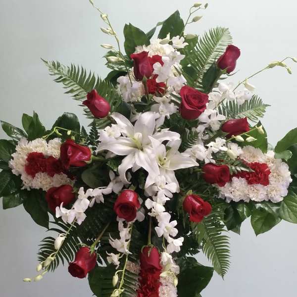 Standing floral cross with red roses, white lilies, and white orchids