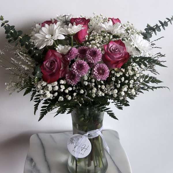 Bouquet of pink roses, white daisies, and purple mums in a glass vase