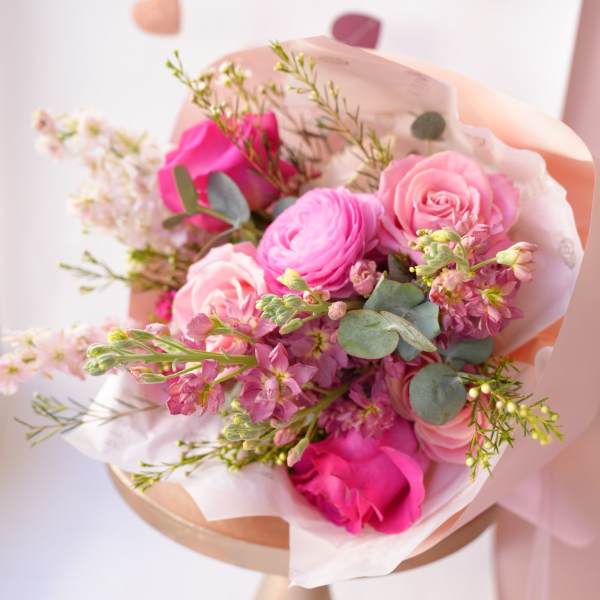 Pink rose and ranunculus bouquet wrapped in pale paper