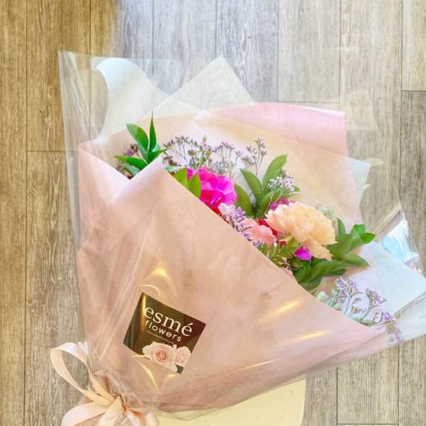 Pink and peach bouquet wrapped in translucent paper with a ribbon