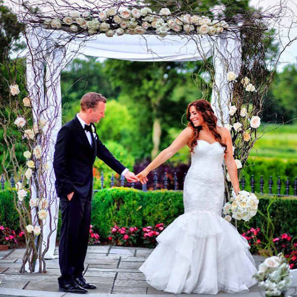 Bride and groom under a floral wedding arch with white roses