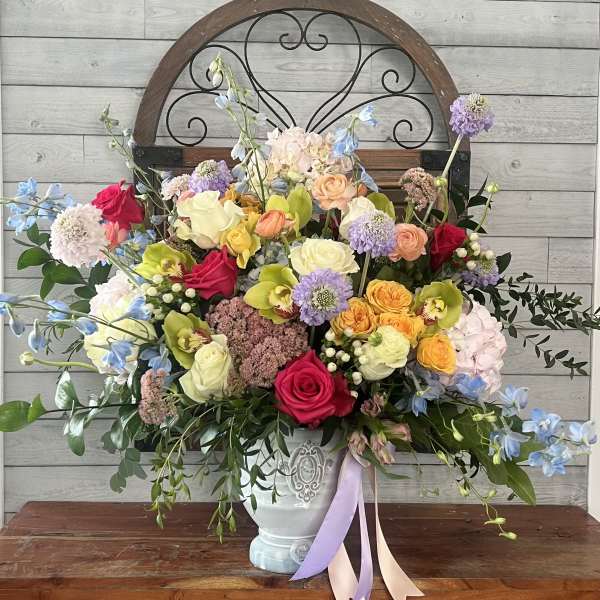 Colorful mixed flower arrangement in a white vase with ribbon tails