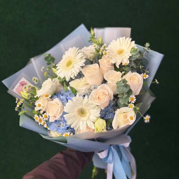Bouquet of cream roses, white daisies, and blue hydrangeas wrapped in pale blue paper