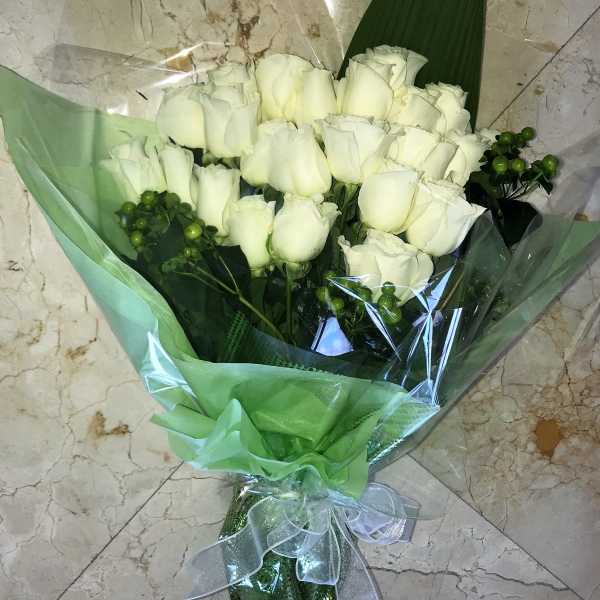 Bouquet of white roses with green berry accents wrapped in green and clear cellophane.