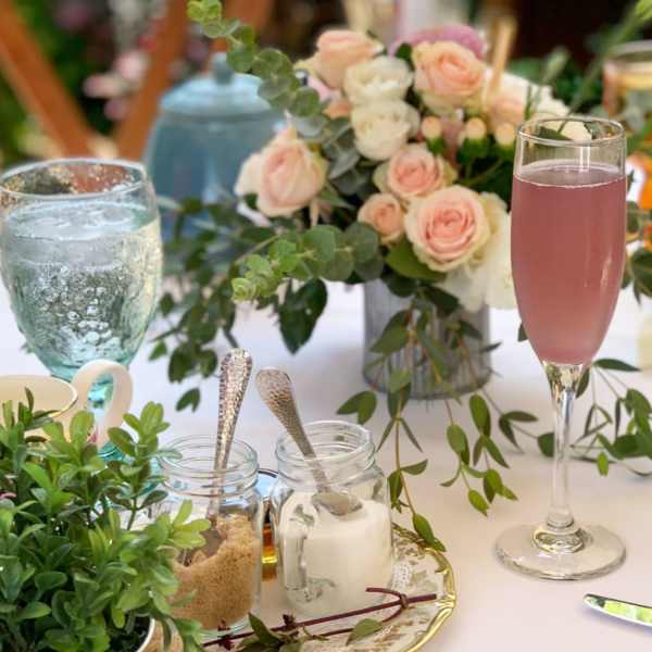 Pastel rose centerpiece with greenery on a table beside drinks and jars