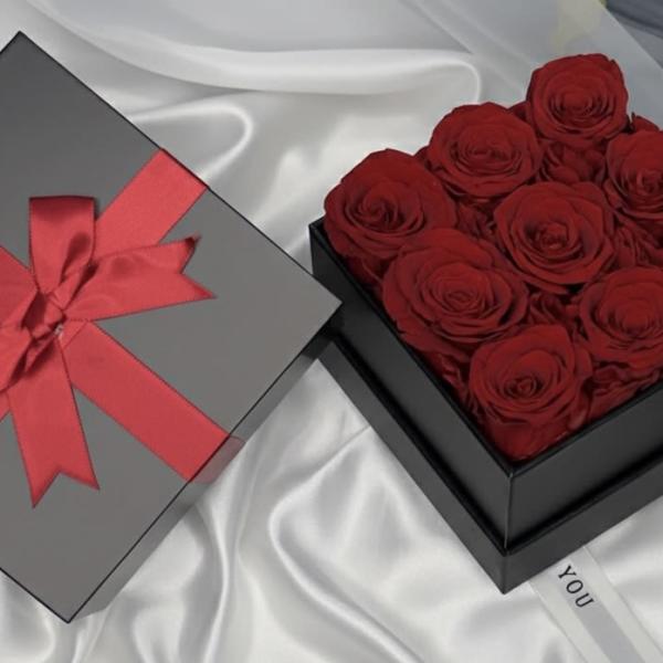 Box of red roses beside a gray gift box with a red ribbon