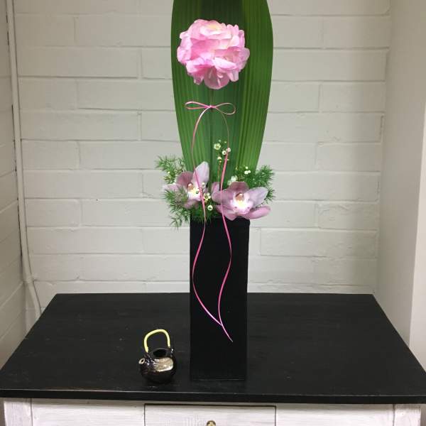 Tall floral arrangement with pink blooms, orchids, and a large green leaf in a black vase