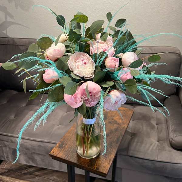 Pink peonies in a glass vase with eucalyptus and blue feather accents