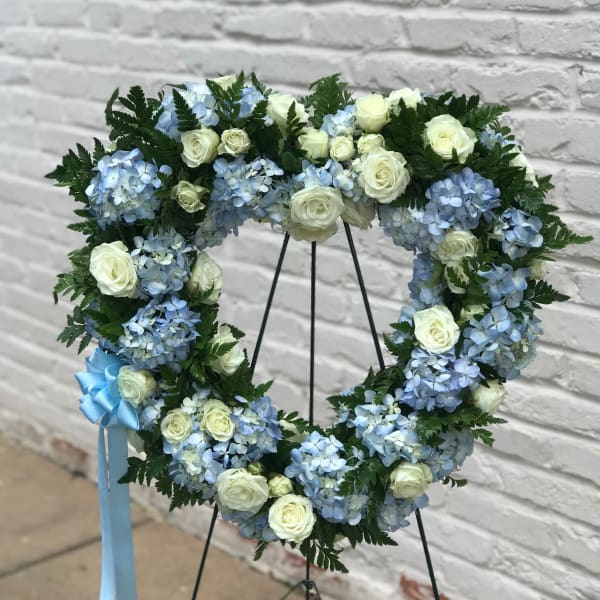 Heart-shaped floral wreath with blue hydrangeas and white roses on a stand