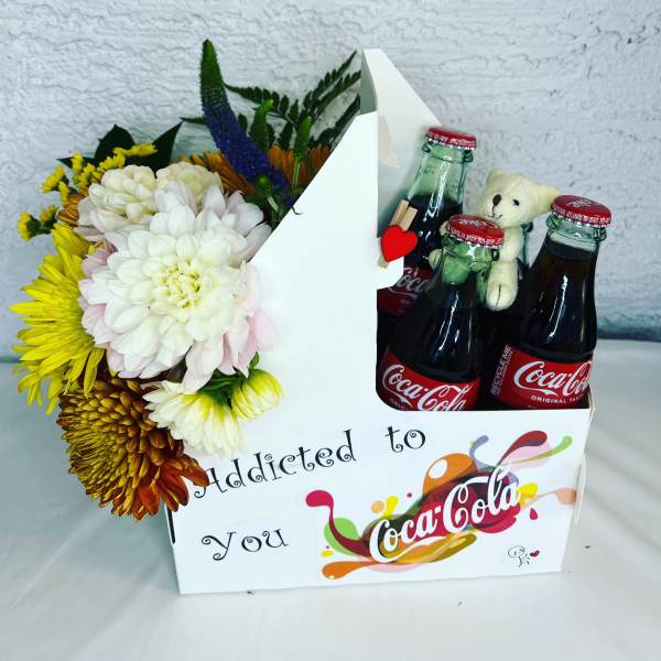 Flower arrangement with Coca-Cola bottles and a teddy bear in a gift box