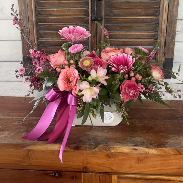 Pink floral arrangement with roses and daisies in a white container