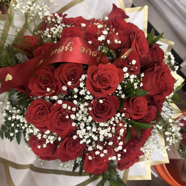 Bouquet of red roses and white filler flowers wrapped in white and gold paper with a red love message ribbon.