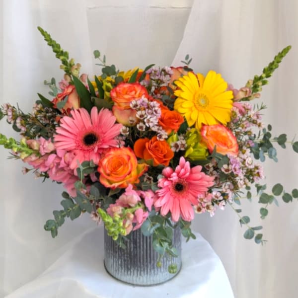 Bright arrangement of pink gerbera daisies, orange roses, and yellow blooms in a ribbed metal vase