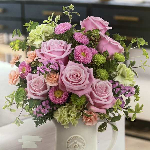 Pink roses and mixed blooms arranged in a white pitcher vase