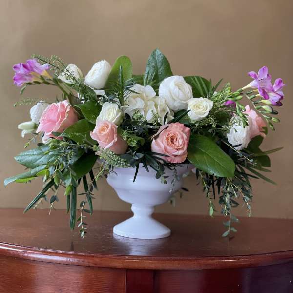 Pink and white roses arranged in a white pedestal vase