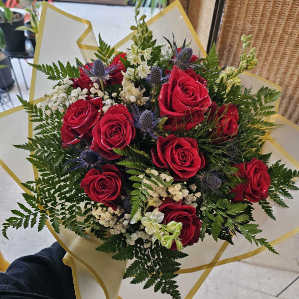Bouquet of red roses with white filler flowers and greenery in gold-trimmed wrap