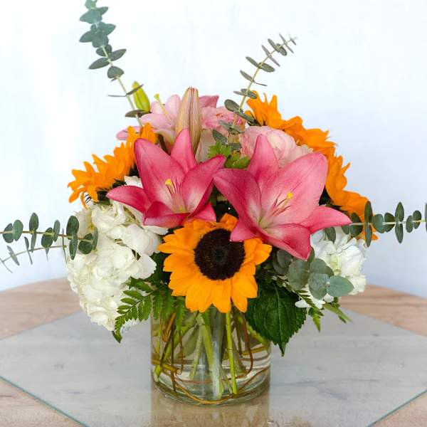 Mixed bouquet with pink lilies, sunflowers, and white hydrangeas in a glass vase