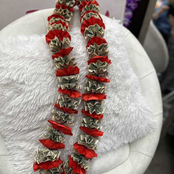 Money lei with red ribbon accents draped over a white chair