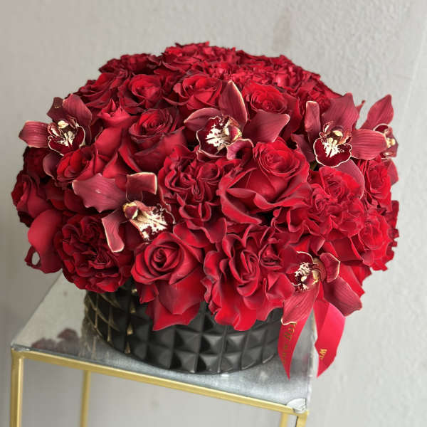 Red rose bouquet with burgundy orchids in a black vase