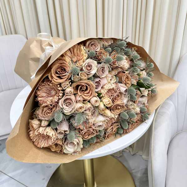 Large wrapped bouquet of muted peach roses and chrysanthemums with thistle-like accents