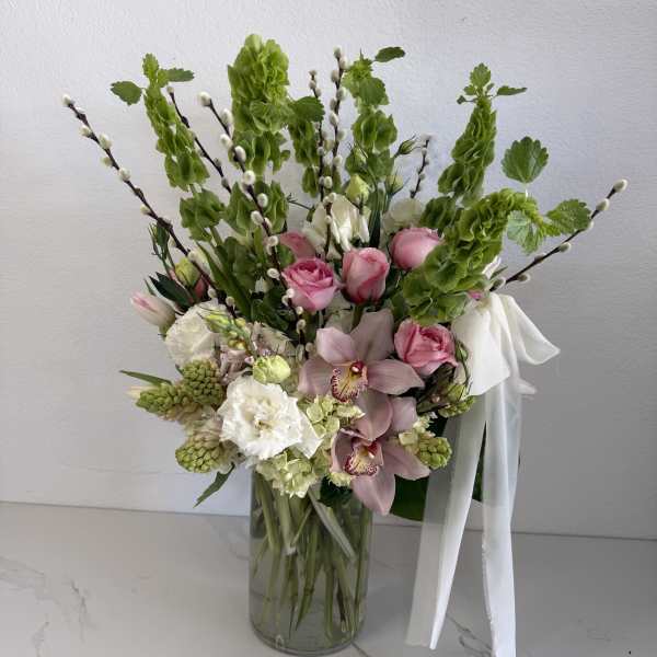 Mixed pink and white floral arrangement in a glass vase with a white ribbon