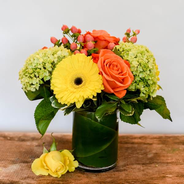 Yellow gerbera and orange roses in a glass vase with green hydrangeas
